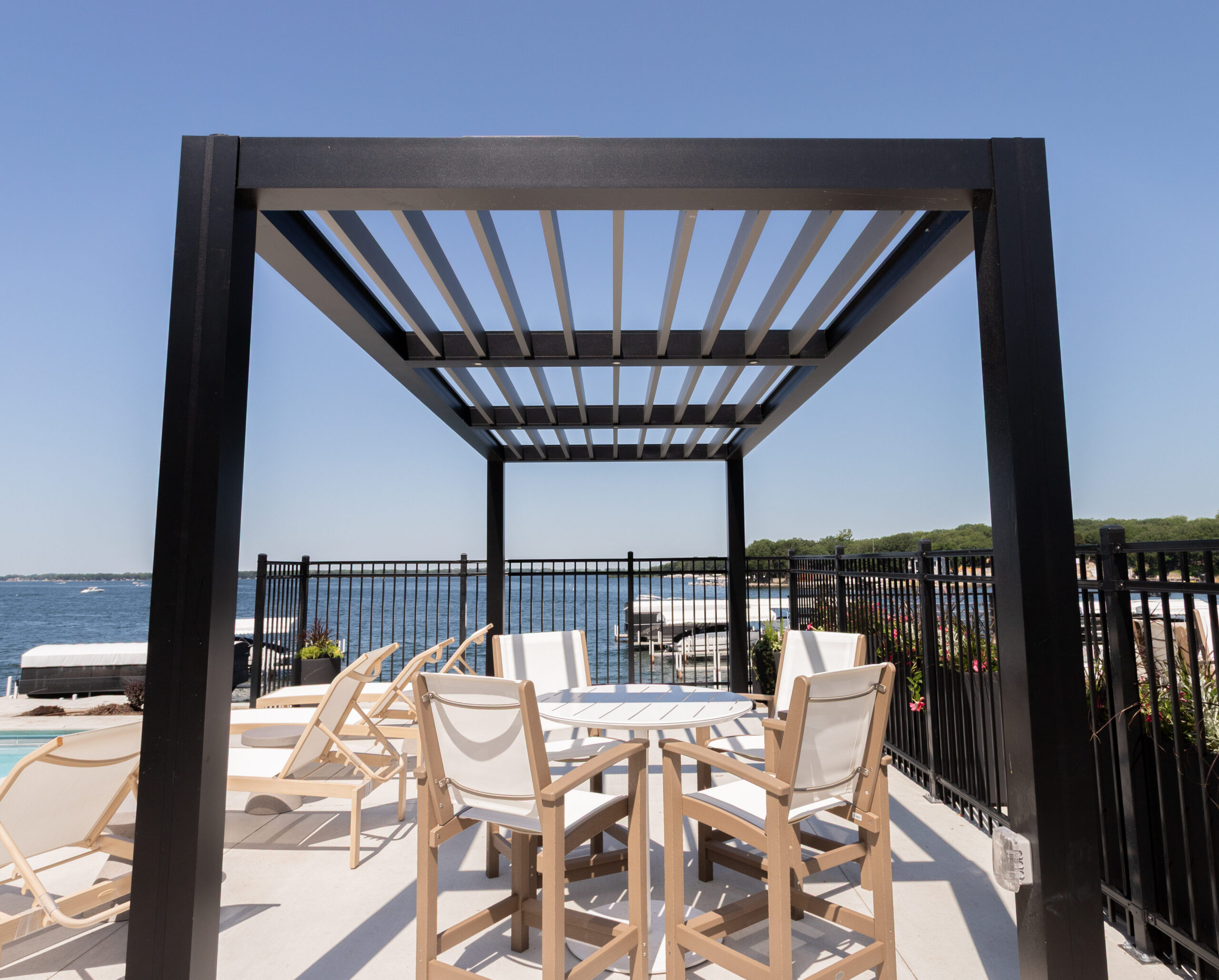 Shade structure made of aluminum with stationary louvers covers a set of chairs around a table.