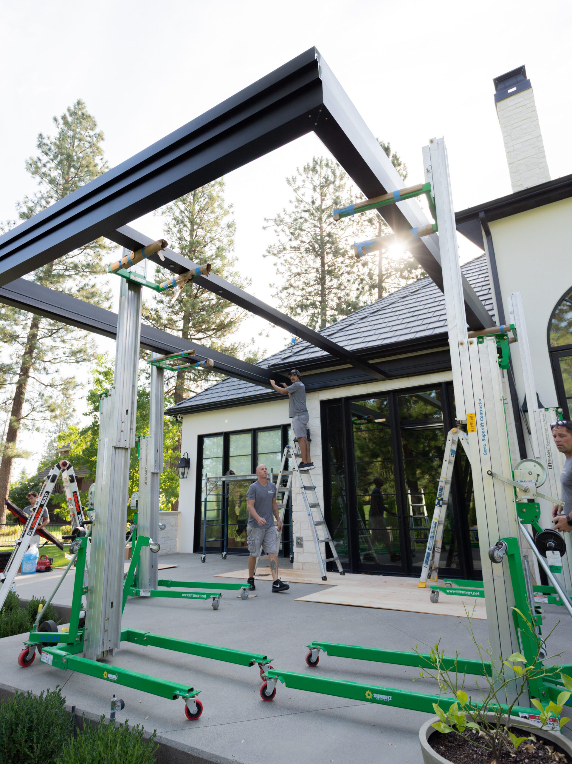 behind-the-scenes of the installation of a custom motorized pergola. The empty frame is lifted into the air.